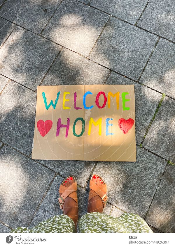 Frau steht vor einem Schild auf dem in bunten Buchstaben „Welcome Home“ geschrieben steht Willkommen willkommen Zuhause welcome home schild Begrüßung Rückkehr