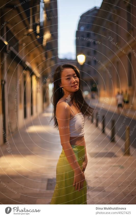 Schöne junge asiatische Frau zu Fuß die Straße der europäischen historischen Stadt in der Nacht mit Straßenlaternen auf. Weiblicher Tourist aus China auf Reisen in Europa. Mode und Stil Konzept.