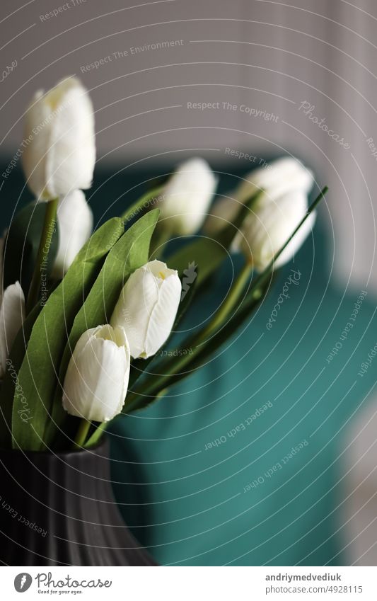 künstliche weiße Tulpen und grüne Blätter in einer schwarzen Vase auf dem Tisch im Haus Interieur. Blume schön Blüte Blumenstrauß Farbe Pflanze