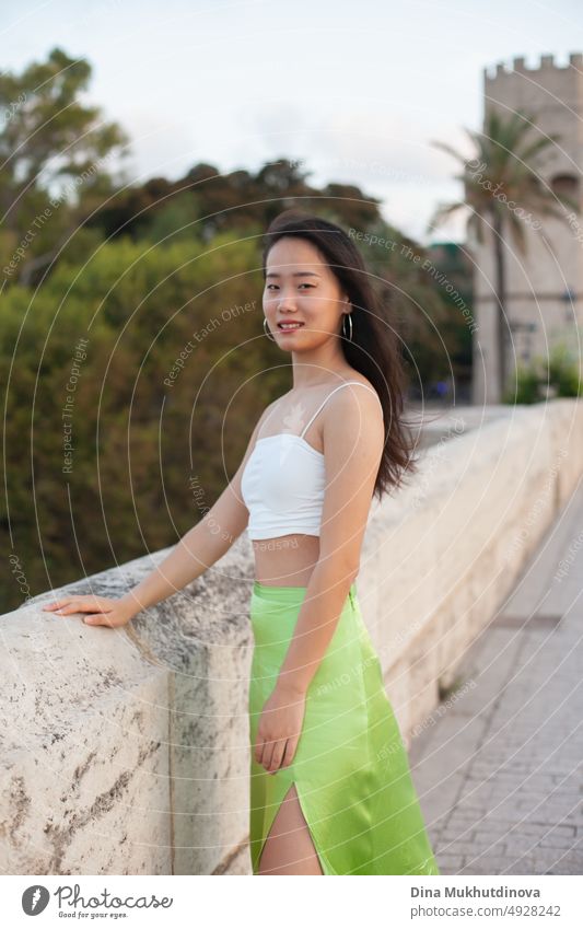 Schöne junge asiatische Frau auf der Straße einer historischen europäischen Stadt mit Palmen. Weibliche Touristin aus China auf Reisen in Europa, lächelnd. Austauschstudentin.
