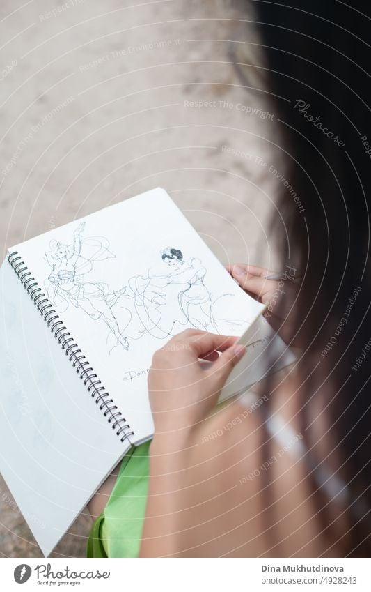 Weibliche Kunststudentin blättert in einem Notizbuch und betrachtet Zeichnungen. Junge asiatische Studentin der Generation Z, die Komposition, Malerei, visuelle Kunst und Zeichnung studiert.