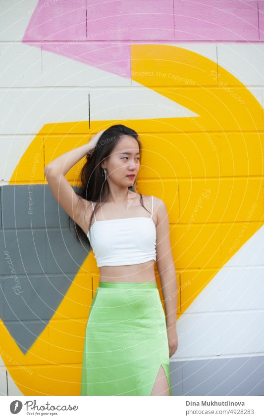 Schönes junges selbstbewusstes asiatisches junges Mädchen posiert vor einer bunten Wand. Weiblicher Tourist aus China auf Reisen in Europa. Austauschstudentin. Mode und Stil Konzept mit asiatischen Modell.