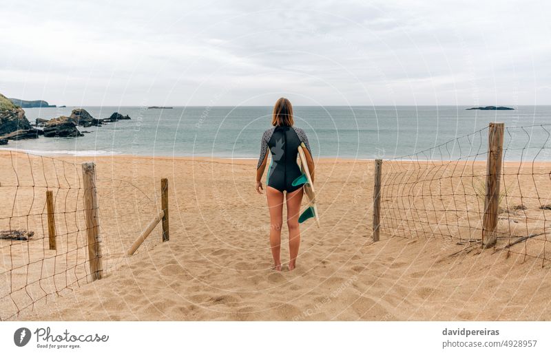 Surferin mit Neoprenanzug und Surfbrett schaut auf das Meer unkenntlich Frau jung Blick MEER Rücken Sand Strand schwimmen tragen Winter Menschen 20s im Freien