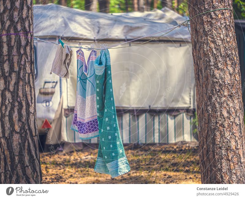 Handtücher an Wäscheleine zwischen zwei Bäumen auf dem Campingplatz. Im Hintergrund  ein Wohnwagen mit Vorzelt. Sehnsucht Zelten reisen Fernweh Fahrzeug Reise