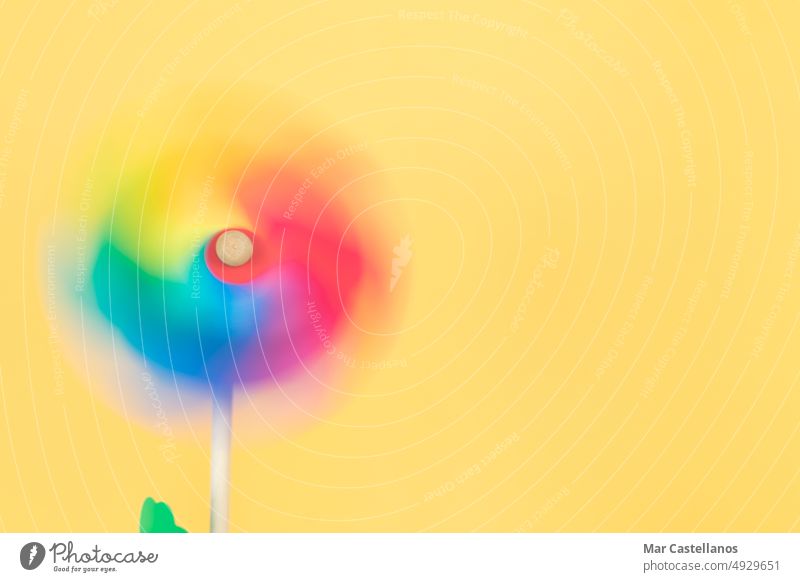 Bewegtes farbiges Windrad auf gelbem Hintergrund. Platz zum Kopieren. Bewegung unkonzentriert Drehung Farbe Kunststoff Sommer Spielzeug Windmühle Spaß Rad blau