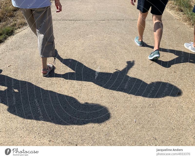 Spaziergänger in der Sonne mit Schatten Spazieren gehen Schattenspiel Mittagszeit Nachmittag Außenaufnahme Spaziergang spazieren Wege & Pfade Mensch Frau Mann