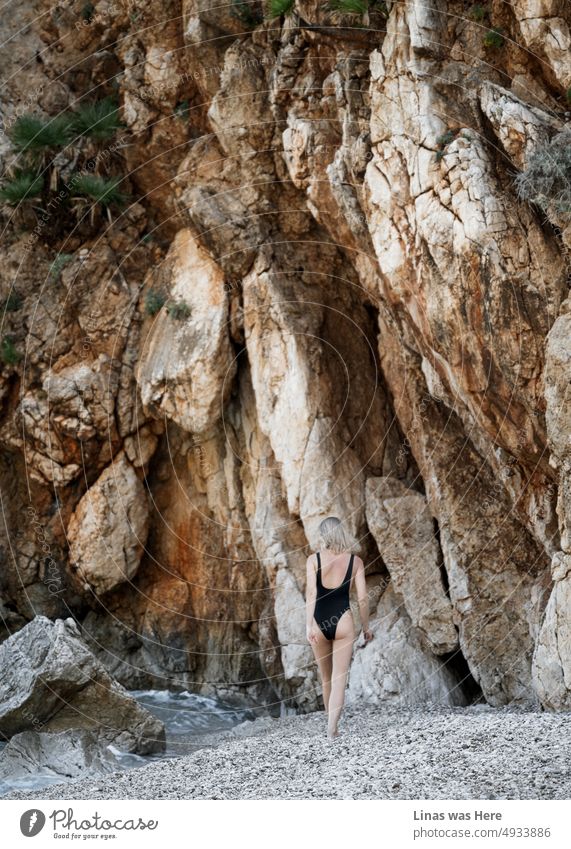 Ein paar hübsche Bewegungen von einem blonden Mädchen im schwarzen Badeanzug. Umgeben von Felsen und Bergen liegt sie an einem schönen Strand. Ein Strand im Zingaro-Nationalpark, Sizilien. Ein Ort, an dem man im Sommer Urlaub machen sollte.
