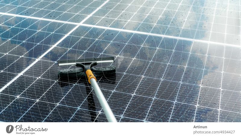 Reinigung eines Solarmoduls mit einem Mikrofasermopp auf einem nassen Dach. Wartung von Solarmodulen oder Photovoltaikmodulen. Nachhaltige Ressource. Solarenergie. Grüne Energie. Technologie für nachhaltige Entwicklung.