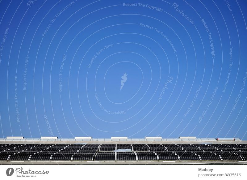 Photovoltaik mit Solarzellen auf dem Dach einer großen Lagerhalle vor blauem Himmel im Sonnenschein in Ibbenbüren im Kreis Steinfurt in Westfalen klimawandel