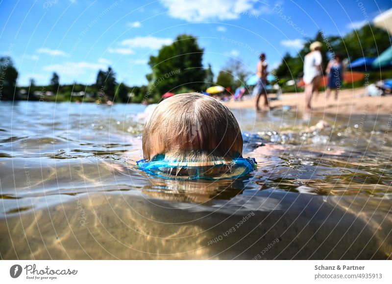 Kind mit Taucherbrille taucht in einem Badesee mit Badegästen am Ufer Urlaub Familie blond tauschen schwimmen Strandurlaub Familienurlaub Familienleben