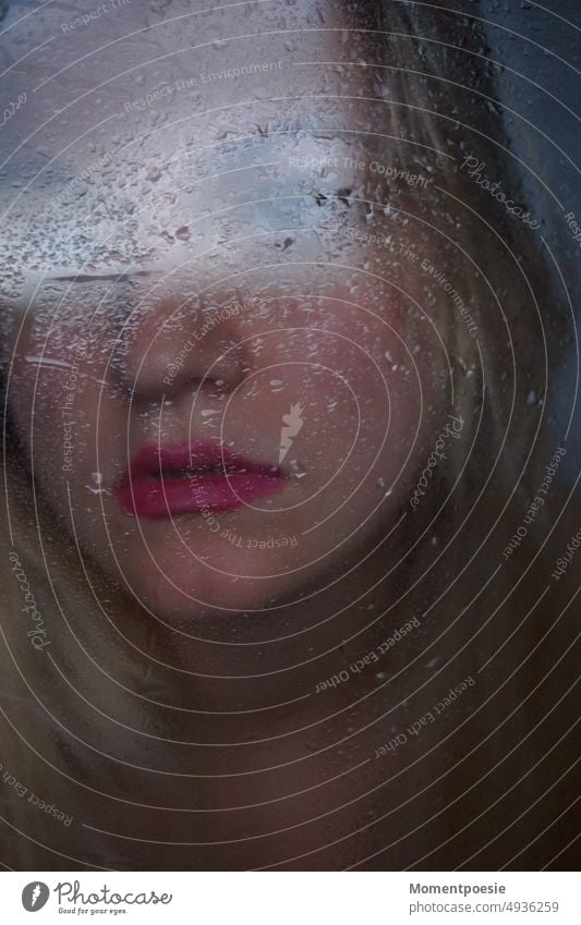 regnerische Aussichten_ junge blonde Frau hinter nasser Fensterscheibe blickt während des Regens nach draußen in die Ferne schlechtes Wetter deprimiert traurig