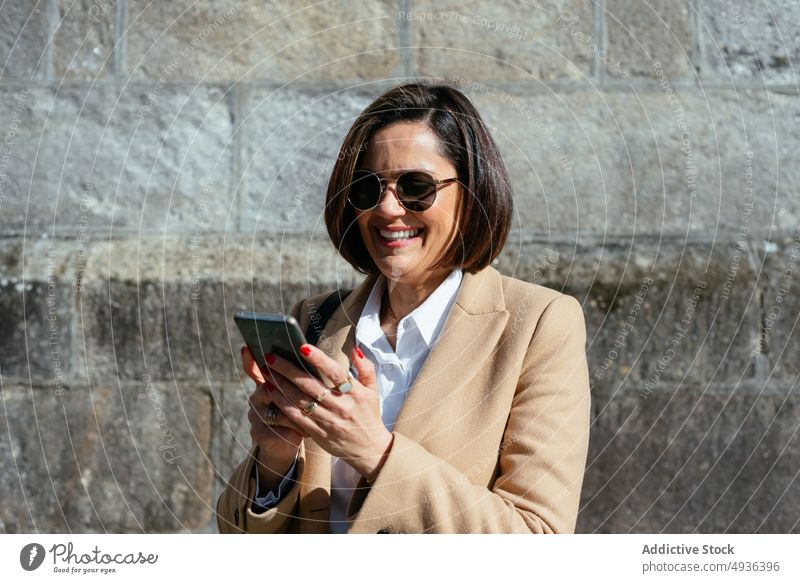 Zufriedene Frau benutzt Smartphone auf der Straße Texten Lächeln benutzend Stil sonnenbeschienen tagsüber Browsen Textnachricht Mobile Telefon Funktelefon
