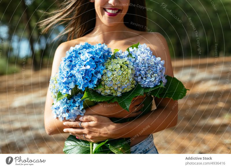 Unerkennbar glückliche verführerische Dame mit Strauß zarter Hortensienblüten im Park Frau Blume Lächeln oben ohne Deckbrust feminin positiv sanft