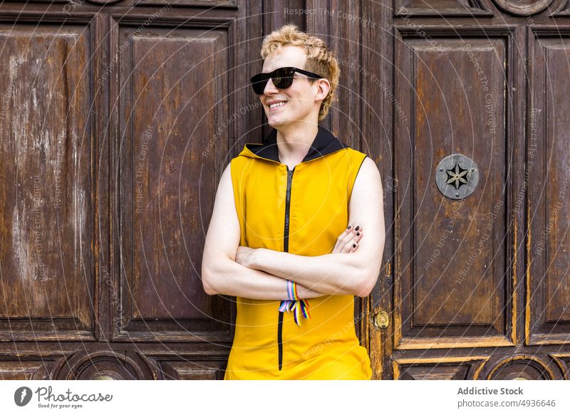 Glücklicher nicht-binärer Mann vor alter Tür Lächeln Transgender nicht binär lgbt Stil Straße Porträt männlich jung Outfit Sonnenbrille gleich Armband Bändchen