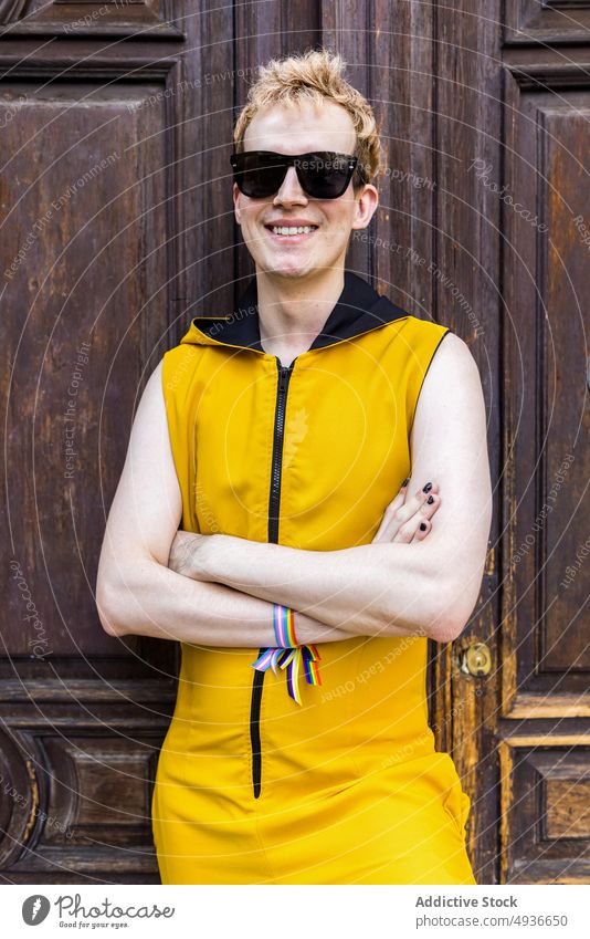 Glücklicher nicht-binärer Mann vor alter Tür Lächeln Transgender nicht binär lgbt Stil Straße Porträt männlich jung Outfit Sonnenbrille gleich Armband Bändchen