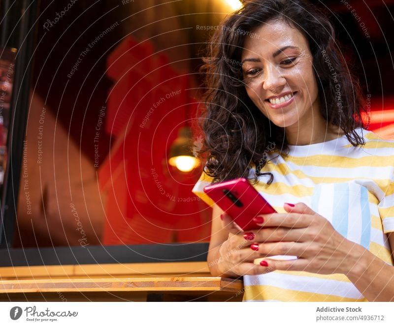 Fröhliche Frau, die in der Nähe eines Cafés auf ihrem Smartphone surft Straße Großstadt Browsen zuschauend benutzend Gespräch Talkrunde Stil heiter positiv