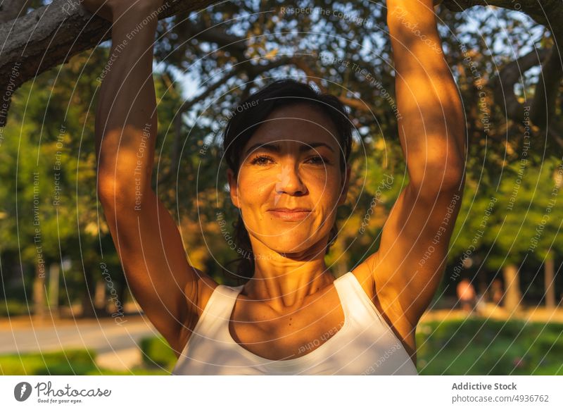 Glückliche Frau hängt an einem Baumzweig Ast hängen Training Sport Park Fitness Gesunder Lebensstil positiv freundlich heiter Inhalt Gesundheit Hobby Lächeln