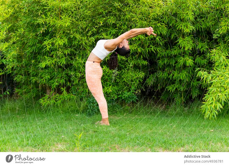 Frau in der Berg-Asana mit erhobenen Armen und Rückbeuge Yoga Berg-Pose Arme hochgezogen Backend Park Training Übung üben ardha chandrasana Baum Form Rasen Zen