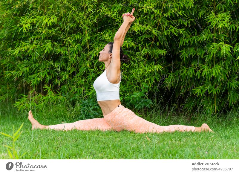 Frau macht Front Spagat im Park Yoga Frontsplits hanumanasana Asana Training Übung üben Gesunder Lebensstil Rasen Arme hochgezogen Barfuß Gras Achtsamkeit Figur