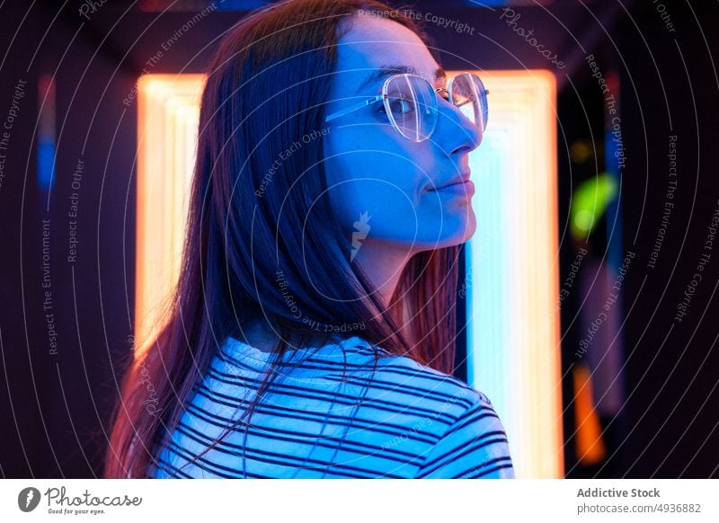 Junge Frau auf dem Flur eines Nachtclubs Gang Wand blau neonfarbig futuristisch leuchten farbenfroh jung lange Haare hell Brille glühen modern Nachtleben