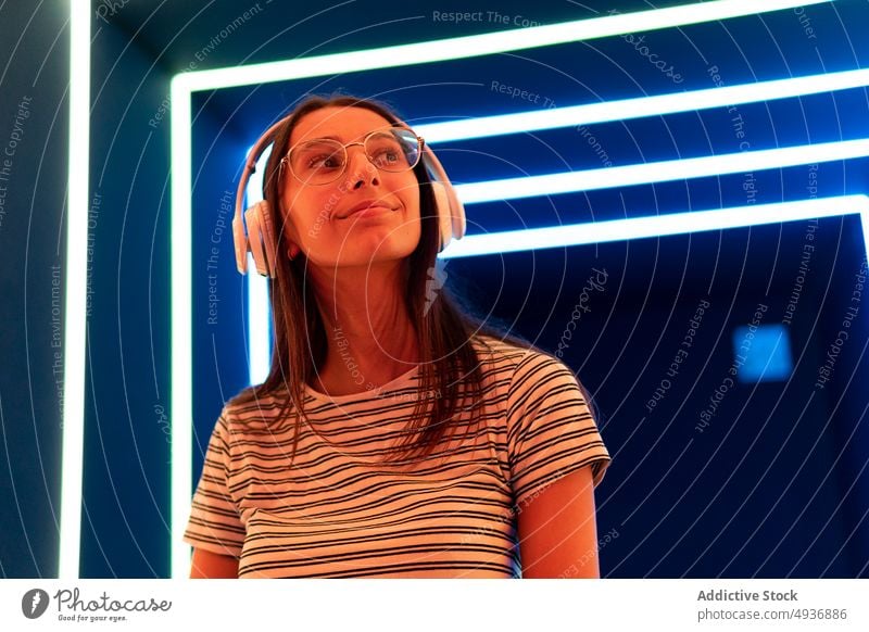 Junge weibliche Melomanin hört Musik in einem futuristischen Korridor Frau zuhören Gang leuchten Kopfhörer meloman Nachtleben jung Klang Apparatur Gesang Audio