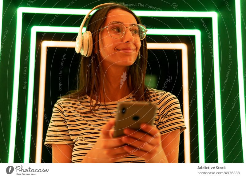 Junge Melomanin benutzt Smartphone in neonfarbenem Korridor Frau Lächeln benutzend Texten Gang grün orange neonfarbig meloman zuhören Musik jung Glück Apparatur