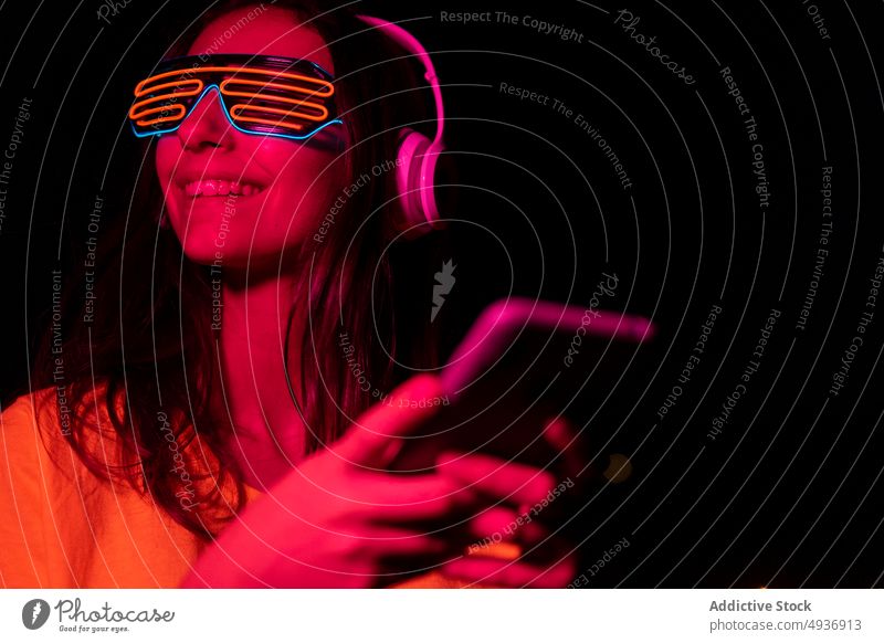 Futuristischer Meloman mit Mobiltelefon Frau Smartphone Texten Lächeln futuristisch Nacht zuhören Musik benutzend Rotlicht jung meloman neonfarbig leuchten