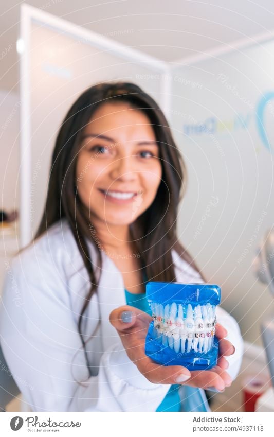 Lächelnder ethnischer Zahnarzt demonstriert Zahnersatz mit Klammern Frau zeigen dental Stomatologie kieferorthopädisch mündlich Freude Arbeit Klinik jung