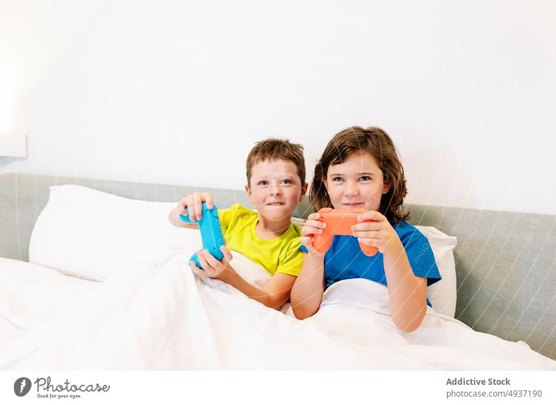 Kinder spielen ein Videospiel im Bett Geschwisterkind Gamepad unterhalten Vergnügen Zeitvertreib Freizeit Hobby Schwester Bruder Junge Mädchen Spiel spielerisch