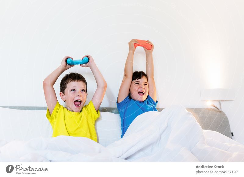 Kinder spielen ein Videospiel im Bett Geschwisterkind Gamepad Arme hochgezogen unterhalten heiter Vergnügen Zeitvertreib Freizeit Lächeln Hobby Schwester Bruder