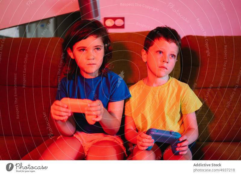 Kinder spielen abends ein Videospiel Geschwisterkind Abend Wohnzimmer unterhalten Vergnügen Zeitvertreib Freizeit Liege Sofa halbdunkel neonfarbig spät Barfuß