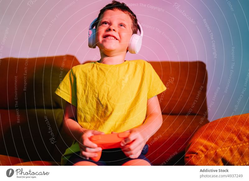 Fröhlicher Junge beim Videospiel Kind spielen unterhalten Vergnügen Zeitvertreib Wohnzimmer aufgeregt Glück positiv heiter Freude zufrieden Kopfhörer genießen