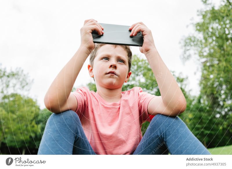 Junge benutzt Smartphone auf Parkwiese zuschauen Video Rasen benutzend Wochenende Sommer Zeitvertreib Kind Apparatur Gerät Funktelefon Gras Internet Kindheit