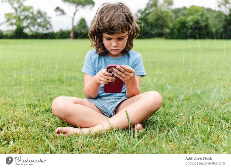 Mädchen benutzt Smartphone auf Parkrasen zuschauen Video Rasen unglücklich benutzend verärgert Wochenende Sommer Zeitvertreib Kind Apparatur traurig Gerät