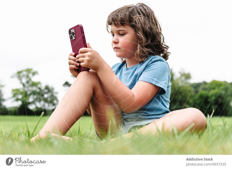 Mädchen benutzt Smartphone auf Parkrasen zuschauen Video Rasen unglücklich benutzend verärgert Wochenende Sommer Zeitvertreib Kind Apparatur traurig Gerät