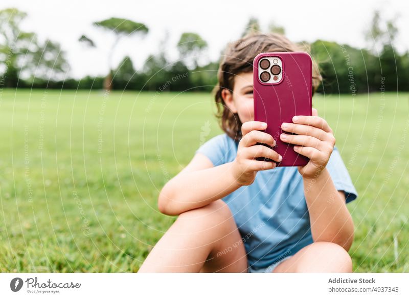 Mädchen benutzt Smartphone auf Parkrasen zuschauen Video Rasen benutzend Wochenende Sommer Zeitvertreib Kind Apparatur Gerät Funktelefon Gras Internet Kindheit