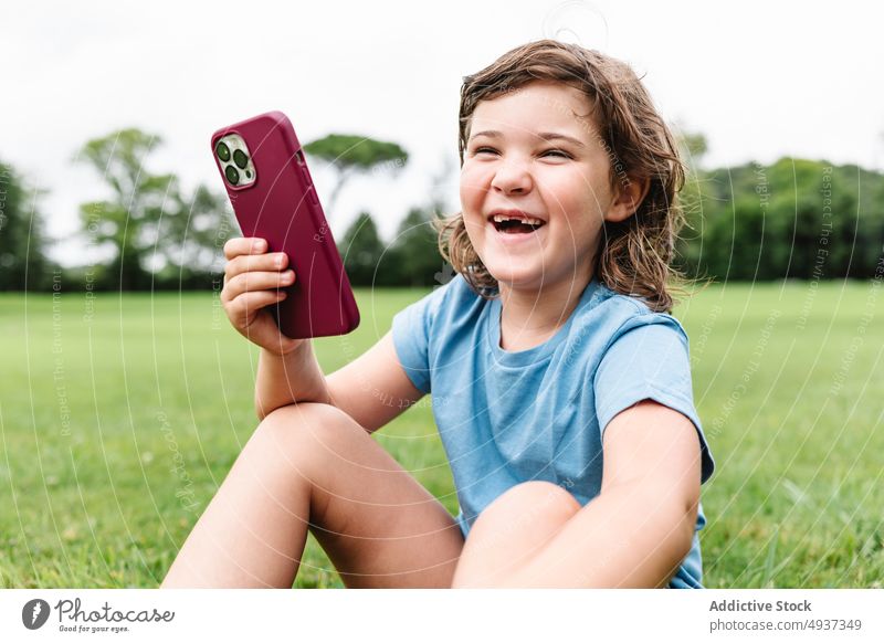 Fröhliches Mädchen mit Smartphone auf einer Parkwiese zuschauen Video Rasen heiter benutzend aufgeregt Sommer Zeitvertreib Glück Kind Apparatur Gerät