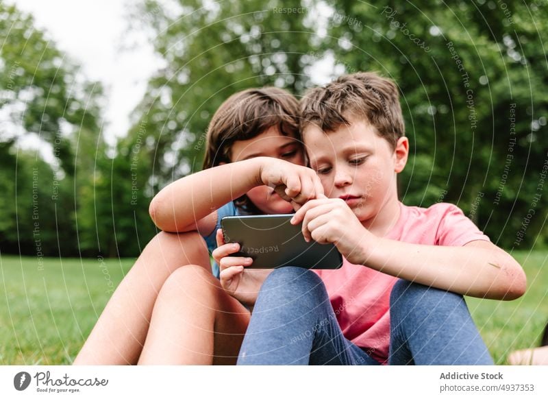 Geschwister nutzen Smartphone gemeinsam im Park Kinder Geschwisterkind Videospiel spielen Zusammensein Wochenende teilen Freundschaft Rasen Zeitvertreib online