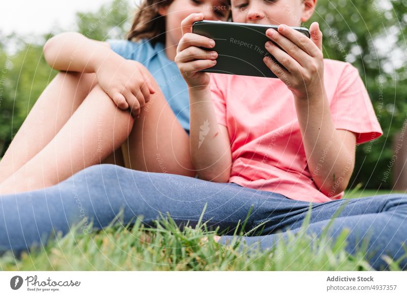 Anonyme Geschwister benutzen gemeinsam Smartphone im Park Kinder Geschwisterkind Videospiel spielen Zusammensein Wochenende teilen Freundschaft Rasen
