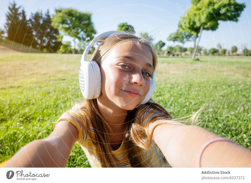Fröhliches Mädchen mit Kopfhörern macht Selfie im Park Teenager Smartphone Fotografie soziale Netzwerke Musik zuhören Inhalt sorgenfrei Moment Gedächtnis Halt
