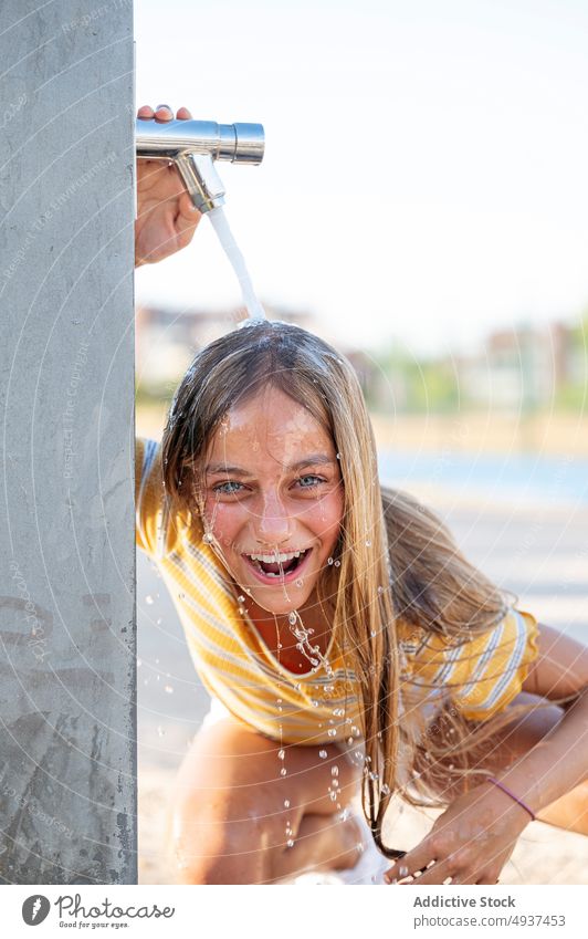 Glückliches Mädchen unter Wasser am Ufer stehend Teenager sorgenfrei Wasserhahn Spaß haben Hafengebiet Stauanlage spielerisch Küste nasses Haar aufgeregt Straße