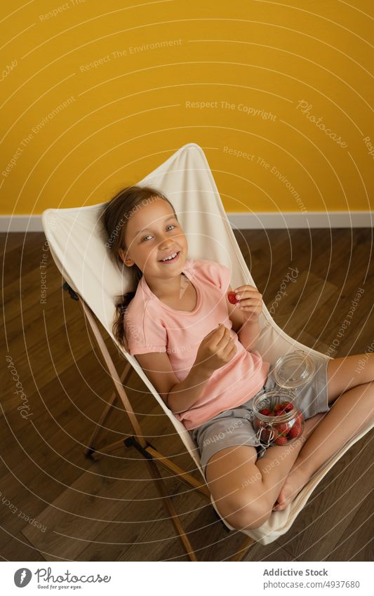 Fröhliches Mädchen isst Erdbeeren auf einem Liegestuhl essen Lächeln heimwärts Wochenende Sommer Glück frisch Kind Glas lässig heiter Beine gekreuzt süß