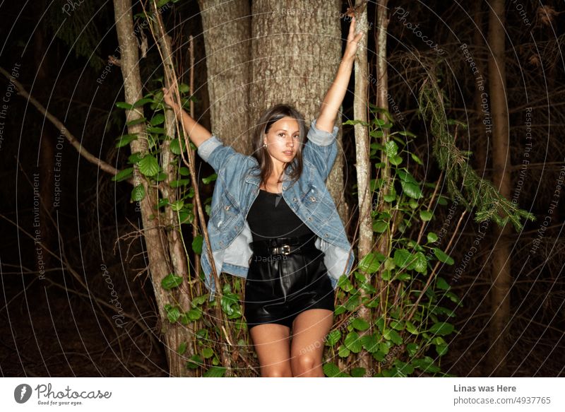 Ein wunderschönes gebräuntes brünettes Mädchen macht es sich im Wald gemütlich. Gekleidet in blauen Jeans und schwarzen Outfit ist sie alle wunderschön aussehen. Flashlight Bild macht das Bild mehr intim.