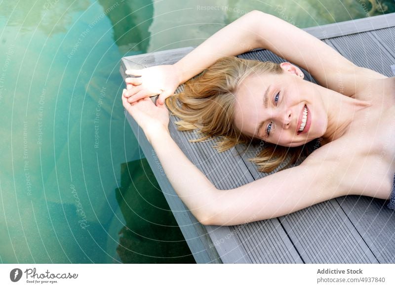 Glückliche blonde Frau, die sich am Pool ausruht ruhen Spa Resort Lächeln Stock Wasser Wochenende Sommer jung Arme hochgezogen Sauberkeit sich[Akk] entspannen