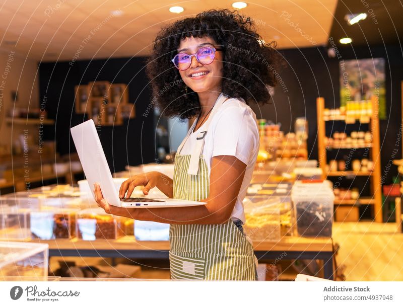 Fröhliche schwarze Verkäuferin beim Inventarisieren von Waren Frau Anbieter Bestandsaufnahme Laptop benutzend prüfen Laden keine Verschwendung