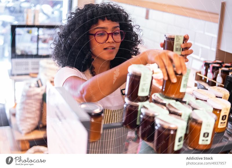 Schwarze Frau arrangiert Marmeladensaucen im Regal eines Geschäfts Saucen Lebensmittelgeschäft einrichten Werkstatt Arbeit umweltfreundlich Kleinunternehmen