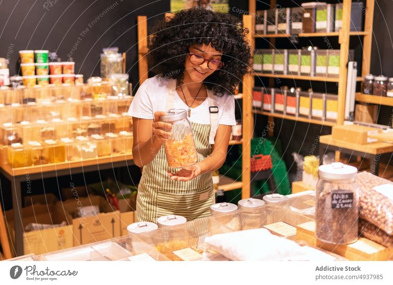 Freundlicher afroamerikanischer Verkäufer mit Trockenfrüchten Frau Lächeln getrocknet Frucht zeigen Container keine Verschwendung Laden Anbieter Porträt jung
