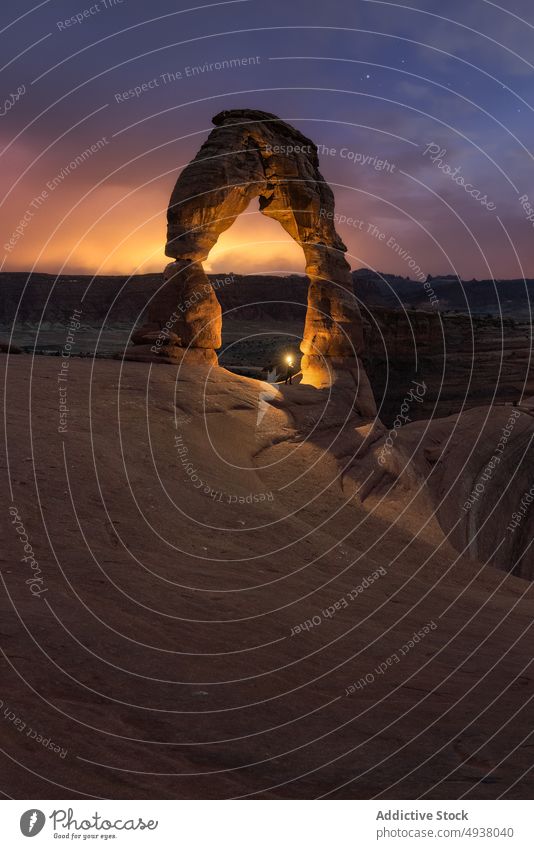 Reisende mit Taschenlampe in der Nähe von Steinbogen gegen Sonnenuntergang Himmel Reisender Bogen Formation sternenklar wüst leuchten wolkig Natur trocken