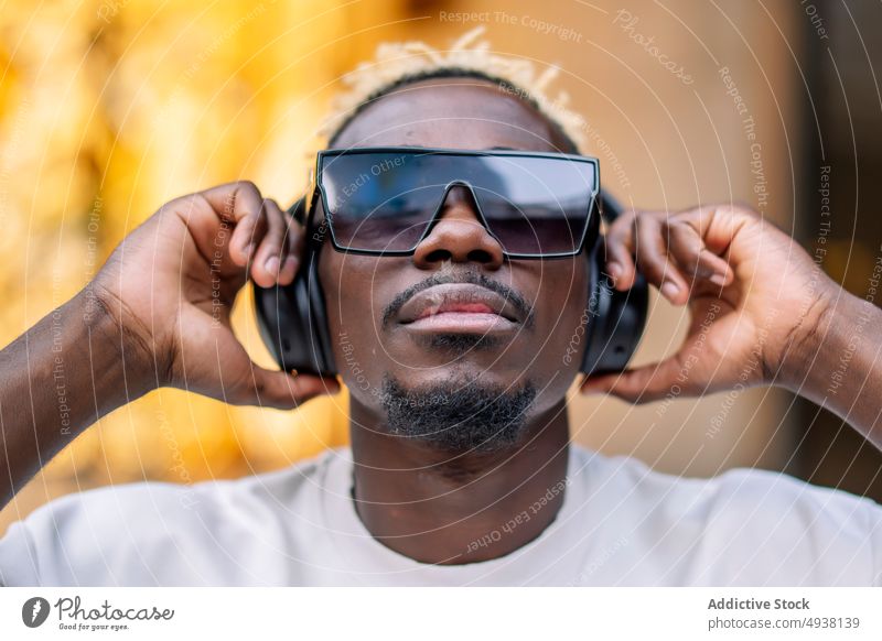 Schwarzer Mann beim Musikhören auf der Straße zuhören urban meloman Glück Kopfhörer ausrichten männlich jung schwarz Afroamerikaner Sonnenbrille ethnisch