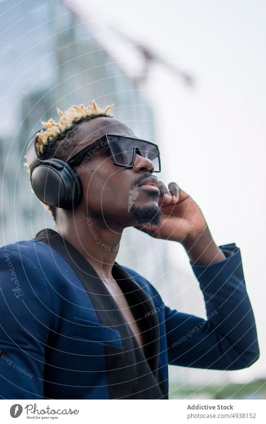 Stilvolle afroamerikanische Meloman, die Kopfhörer einstellt Mann zuhören Musik Straße urban ausrichten ernst modern männlich jung schwarz Afroamerikaner